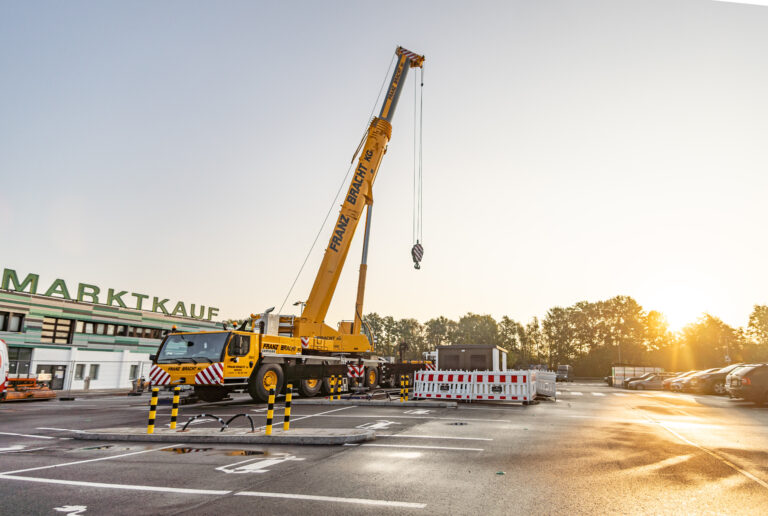 Montage einer Kompaktstation auf dem Parkplatz von Marktkauf Ein großer gelber Mobilkran hebt bei Sonnenaufgang eine Kompaktstation auf dem Parkplatz eines Marktkauf-Marktes an.