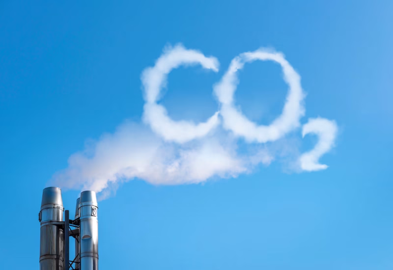 Industrieller Schornstein mit CO₂-Schrift aus Rauch – Symbolbild für Emissionen und CO₂-Reduzierung durch BESS-Batteriespeicher von Faber E-Tec