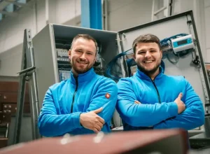 Zwei lächelnde Mitarbeiter der Faber E-Tec GmbH in blauer Arbeitskleidung